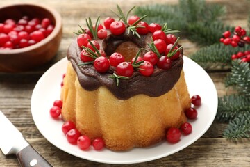 Delicious Christmas cake with chocolate glaze, cranberries, rosemary and fir tree branches on wooden table, closeup