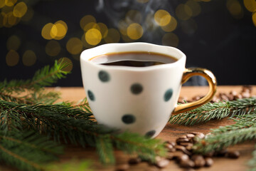 Aromatic coffee in cup, beans and fir tree branches on wooden table against black background with blurred lights, closeup. Bokeh effect