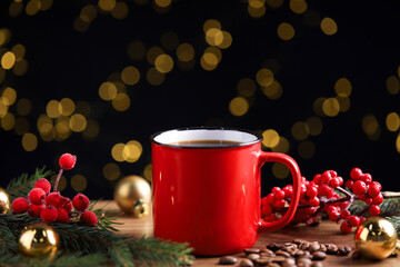 Aromatic coffee in red mug, beans, berries and fir tree branches on wooden table against black background with blurred lights, closeup. Christmas greeting card