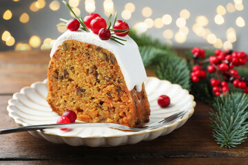 Slice of tasty Christmas cake with cranberries served on wooden table against blurred lights, closeup