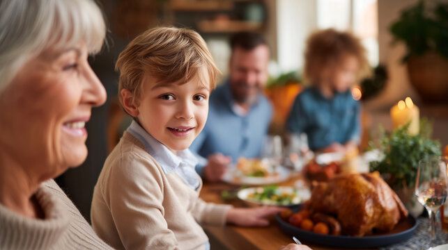 Grandmother and grandson smiling together at thanksgiving dinner table with family. Joyful intergenerational gathering celebrating holiday with roasted turkey. Warm family bonding moment at home.