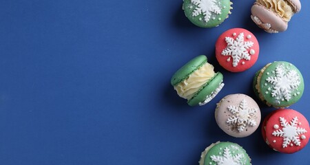 Christmas macarons decorated with snowflakes on blue background, flat lay. Space for text