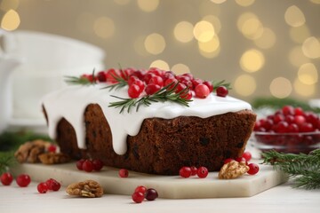 Tasty Christmas cake with cranberries, walnuts, rosemary and fir on white table against blurred festive lights, closeup. Bokeh effect
