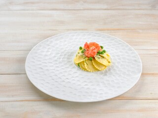 A beautifully arranged dish features homemade ravioli filled with ricotta, adorned with fresh shrimp and bright green peas on a unique white plate