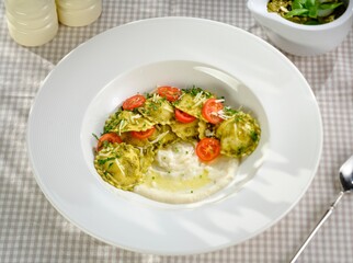 In a cozy dining setting, colorful fresh pasta is served in a large bowl. Topped with cherry tomatoes, herbs, and olive oil, it looks inviting and delicious, perfect for sharing