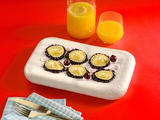 Colorful appetizers are arranged neatly on a unique white platter, accompanied by two glasses of fresh orange juice. The vivid red background adds excitement, creating a joyful dining experience
