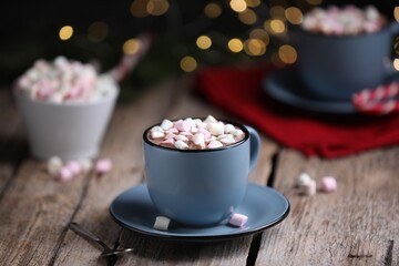 Tasty cocoa with marshmallows on wooden table against blurred Christmas lights, closeup