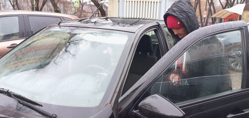 A woman in a hooded jacket gets into a car in an urban area