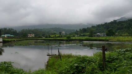 Serene Lake Landscape Surrounded by Greenery and Misty Mountains Under Cloudy Monsoon Sky
