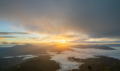 Fototapeta premium Sunlight breaking through clouds over mountain range and sea of mist, beautiful morning nature view.