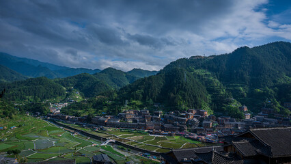 Panoramic view of Xijiang Miao Village surrounded by mountains and rice fields in Guizhou, China.