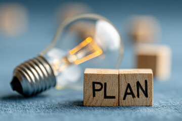 Conceptual Image of a Light Bulb and Wooden Blocks Spelling the Word Plan on a Blue Textured Background, Symbolizing Strategy and Creative Thinking