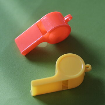 Una toma de cerca de dos silbatos de color amarillo y anaranjado en un fondo amarillo y verde