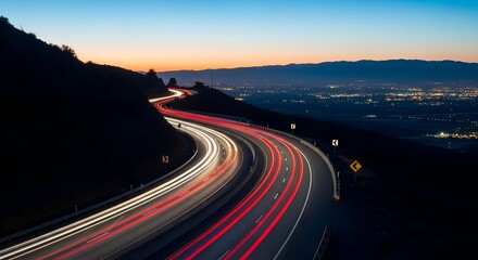 Long exposure highway traffic light trails winding through mountains at dusk with city lights below