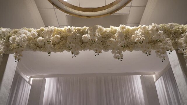 An elegant wedding arch lavishly decorated with white orchids and roses. This luxurious and romantic setup is perfect for wedding ceremonies, event planning, and celebratory concepts.