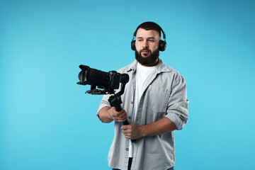Videographer using gimbal stabilizer with camera on light blue background. Space for text © New Africa