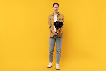 Fototapeta premium Videographer using gimbal stabilizer with camera on yellow background