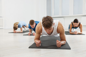 Group of people doing plank exercise on fitness mats in gym, selective focus