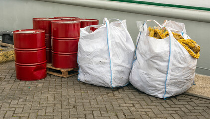 two white jute bags with rope and five red oil drums are outside on the quay of the harbour