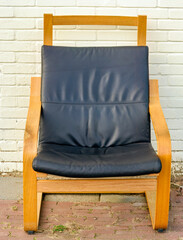 wooden armchair with a black leather cushion stands outside in front of a cream-colored painted wall