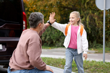 Father taking his daughter to school and giving high five near car outdoors