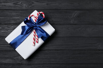 Obraz premium Decorated Christmas gift with candy canes on black wooden background, top view. Space for text