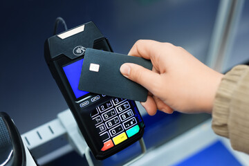 Hand holding a black credit card near a modern black POS terminal for a contactless NFC payment transaction.