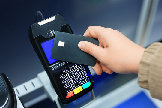 Hand holding a black credit card near a modern black POS terminal for a contactless NFC payment transaction.