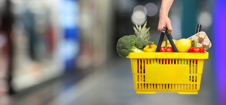 Customer holding shopping basket with different food products at supermarket, closeup. Banner design