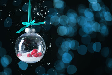 Christmas ball with snow and berries inside against blurred lights on dark background