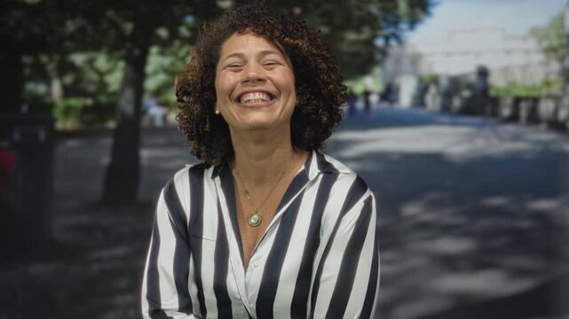 Middle aged hispanic woman touching her cheek and smiling on a sunlit city street; happiness.