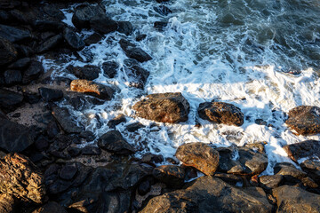 Ocean waves crashing against the beach rocks, light reflecting on the water.