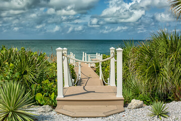 Wood boardwalk with white rope fence entrance to beach 
