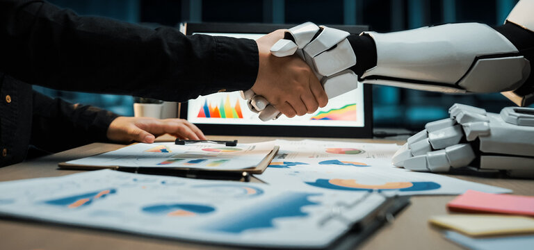 A human and robot engage in a handshake, representing collaboration in a modern office. This image captures the essence of technology working alongside people effectively.Noogenesis