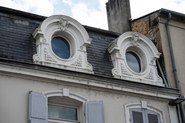 The intricate design of two circular windows on a building showcases ornate details against a blue sky. Sunlight highlights the craftsmanship of this historic structure.