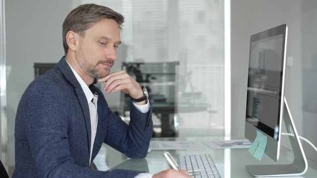 Businessman in a blue jacket thinking and brainstorming ideas while working on computer and taking notes in modern office. Business people concept