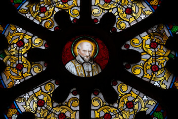 This stained glass window showcases Saint Vincent de Paul, surrounded by intricate floral designs. Located in the Basilica of Notre-Dame-de-Buglose, Landes department.