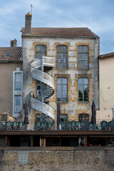 A restaurant terrace in Mont de Marsan features tables with chairs and a unique spiral staircase on the building. The inviting space is perfect for enjoying meals outdoors.
