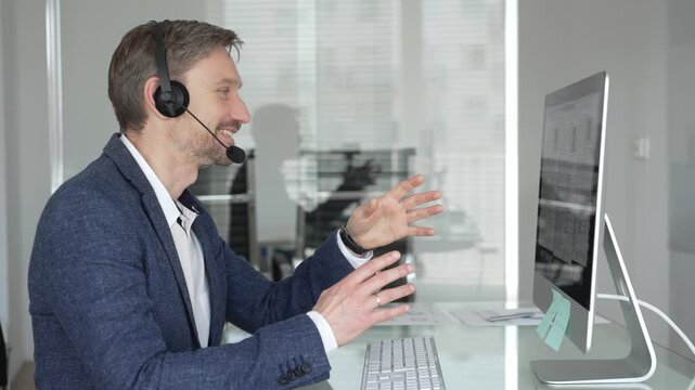 Man in headset talking during online video call, working in office, consulting remote customers, providing technical support. Business people concept