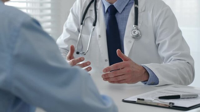 Male doctor explaining diagnosis, gesturing hands to patient during consultation in well lit clinical setting. Medicine and health care concept - Powered by Adobe