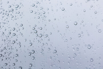 Close-up of a rain-covered window with delicate droplets and a soft, cloudy white sky in the background, creating a calm and minimal atmosphere.