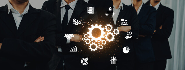 A group of business professionals in suits stands confidently, surrounded by glowing gears and technology icons symbolizing innovation and teamwork in a corporate setting. Trope