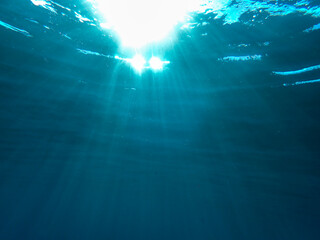 Dark blue ocean surface seen from underwater. Abstract waves underwater and rays of sunlight shining through, Sun light rays undersea deep, Underwater background with sea bottom, Mediterranean sea.