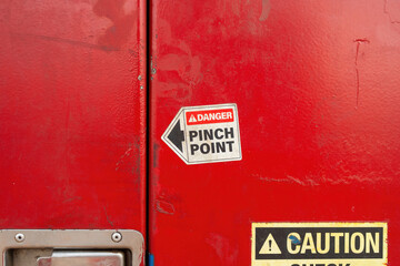 Warning sign "Pinch Point" sticker on metal toolbox doorknob, using to identify hand injury hazard at the workplace. Close-up with selective focus. 