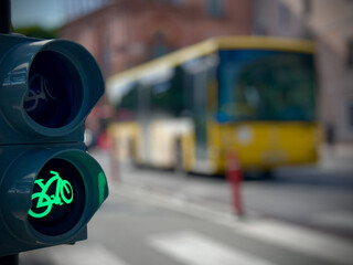 Closeup of bicycle traffic light showing illuminated green cycling symbol on urban street with blurred road background and bright daylight