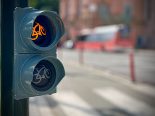 Closeup of bicycle traffic light showing illuminated green cycling symbol on urban street with blurred road background and bright daylight