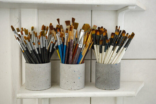 Collection of paintbrushes organized neatly in concrete holders on a wooden shelf in a bright studio