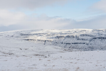 A mountain range is covered with snow during winter under cloudy skies.