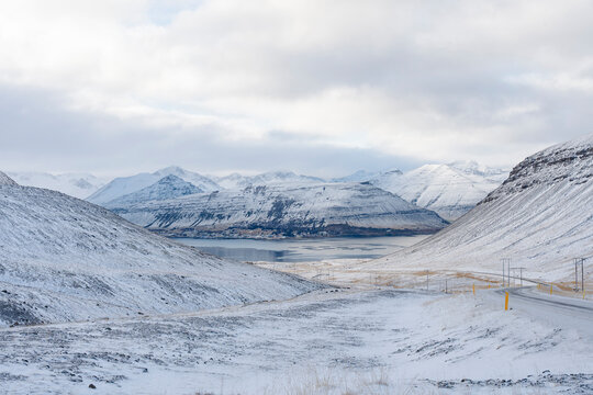 A snow covered valley leads to mountains and a lake on an overcast day. - Powered by Adobe