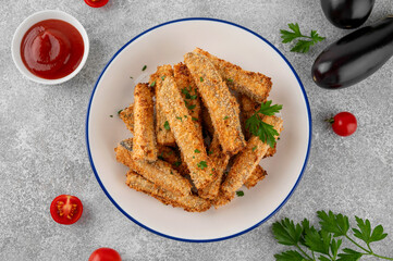 Baked crispy eggplant sticks served with tomatoes sauce on a plate on a gray concrete background. Vegetarian healthy dish. Selective focus